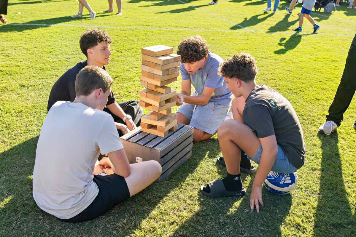 Four students playing giant Jenga on the grass