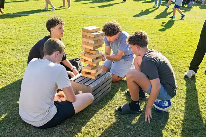 Four students playing giant Jenga on the grass